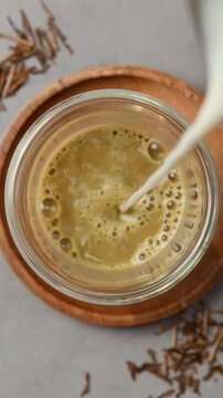 Oat milk pours into hojicha tea in clear glass, blending with roasted tea and forming creamy foam during latte preparation.
