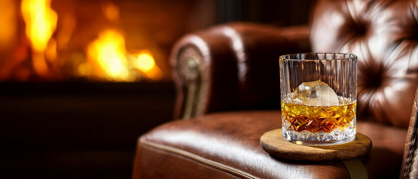 Single malt whisky in crystal glass with ice ball and blurred lounge background banner.