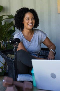 African American woman speaking into condenser microphone while recording on laptop in home studio
