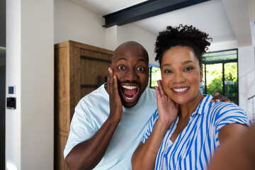 Fototapeta premium African American couple smiling and posing for selfie in modern living area holding smartphone
