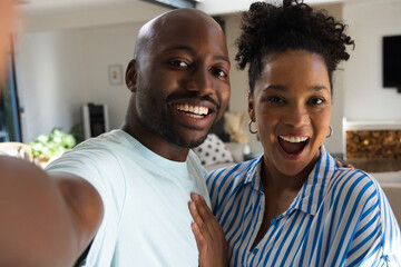 Fototapeta premium African American couple taking selfie, posing in living room with smartphone and patterned cushions