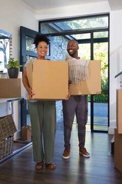 African American couple smiling and carrying moving boxes at modern home entry with knit throw