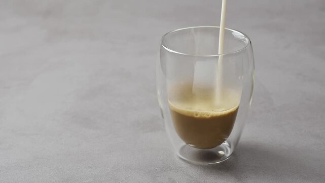 Oat milk pours into hojicha in clear glass, blending with roasted tea and creating creamy foam during latte preparation.