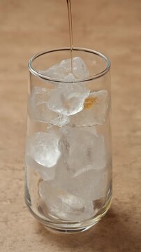 Golden syrup slowly pours over clear ice cubes in a glass, adding sweet flavor before preparation of a refreshing iced drink.