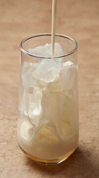 Cold oat milk pours over ice and golden syrup in a clear glass, creating a creamy base for a refreshing iced latte drink.