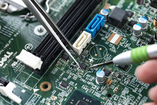 Technician repairing computer motherboard with soldering iron and tweezers