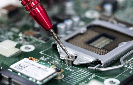 Screwdriver tightening screw on computer motherboard during electronic repair