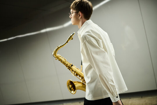 Young adult Caucasian male street musician walking with saxophone in urban underpass. Image suitable for music education marketing, artistic performance promotion, or cultural event advertising