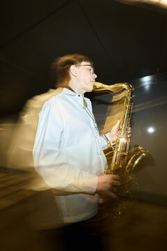 Vertical image of young adult Caucasian man playing saxophone in underpass, motion blur effect showing street performance, perfect for music event promotion or cultural editorial