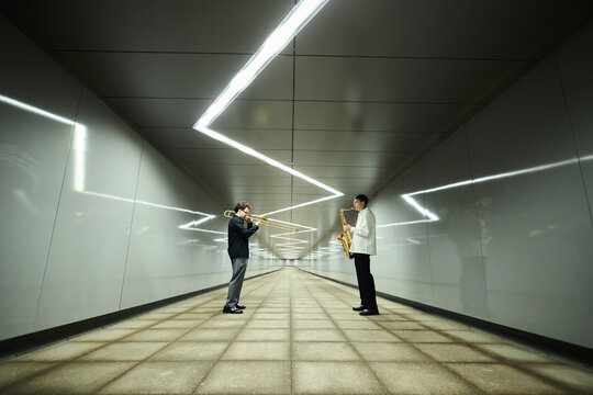 Two young Caucasian male street musicians playing saxophone and trombone in modern pedestrian underpass. Image suitable for urban culture and music education marketing campaigns