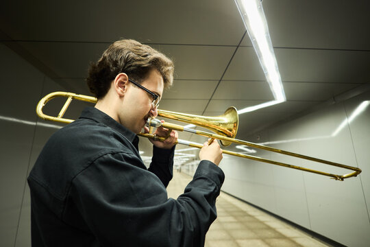 Young adult Caucasian man playing trombone in underground pedestrian tunnel, performing as street musician. Image suitable for music education and urban culture marketing campaigns