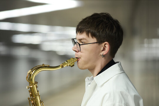 Young Caucasian man playing saxophone in subway station, performing as street musician. Image suitable for promoting urban culture, music education, or busking lifestyle, side view