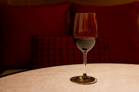 Glass of red wine on a table with red cushions in the background.