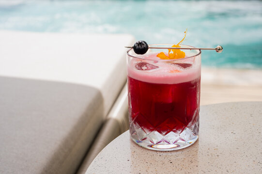 Red cocktail with fruit garnish on a table by the pool.