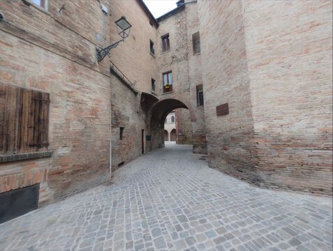 Scorcio di un borgo medievale con un antico arco in pietra, pavimentazione in ciottoli e storici edifici in mattoni a vista