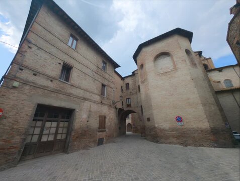 Scorcio di un borgo medievale con un antico arco in pietra, pavimentazione in ciottoli e storici edifici in mattoni a vista