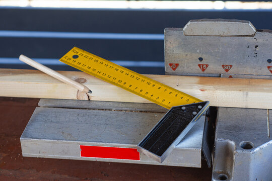 Yellow try square ruler, wooden pencil and plank on miter saw table. Carpentry measurement, precision wood cutting and construction workshop concept for DIY, industrial marketing.