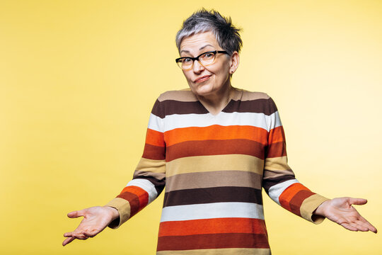 Woman shrugging with open hands, expressing confusion and uncertainty against a bright yellow studio background