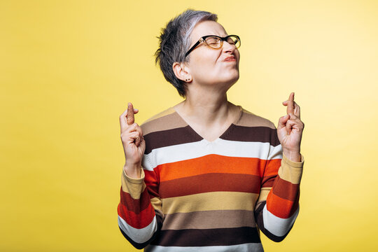 Woman with crossed fingers expressing hope and anticipation on a yellow background, symbolizing superstition and good fortune