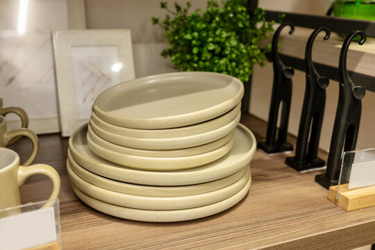 Stack of beige ceramic plates on wooden shelf in kitchen setting