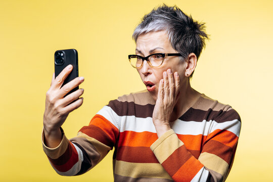 Senior woman with gray hair receiving surprising news on her mobile phone, expressing shock with facial expression
