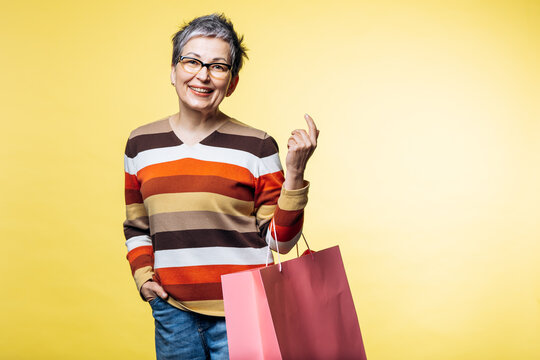 Happy smiling adult female carrying shopping bags ready for purchases or gifts against a vibrant yellow background