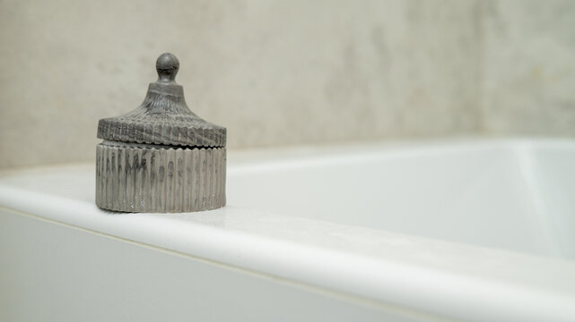 Elegant grey decorative container on white bathtub edge in minimalist bathroom