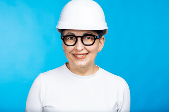 Mature woman architect or construction manager in a safety helmet, confidently smiling against a blue background