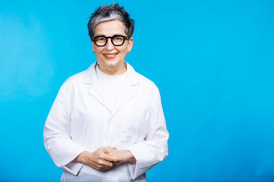 Cheerful female doctor or scientist with short grey hair and glasses smiling, wearing a white lab coat on blue background