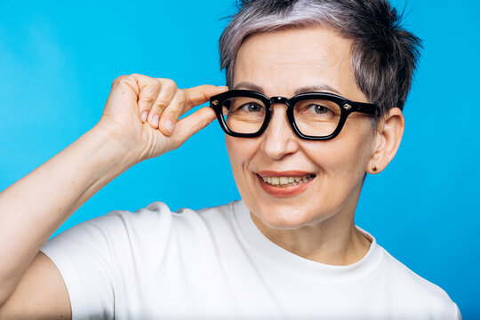 Senior woman with short grey hair and glasses smiling on a blue background, representing clear vision and self-assurance