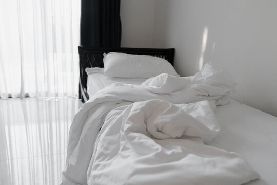 messy blanket on clean white bed and white pillow with morning light  in bedroom of house, resort or hotel, in soft focus