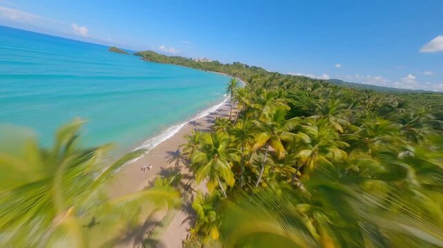 Aerial view gliding along a pristine tropical beach coastline with turquoise water and palm trees.