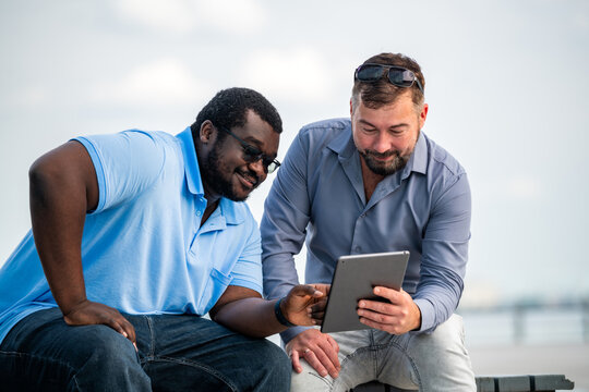 Two diverse male friends using a digital tablet outdoors