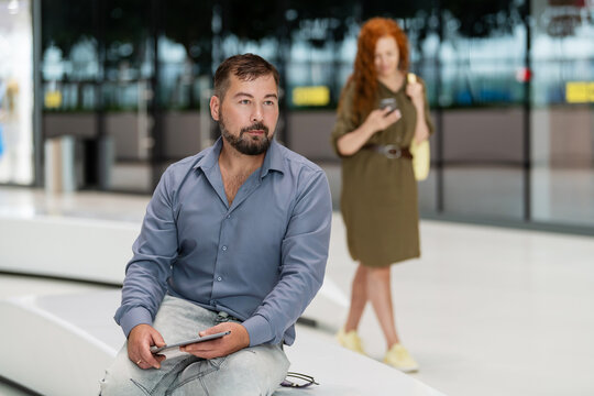 Man with tablet waiting on a bench in a modern public space