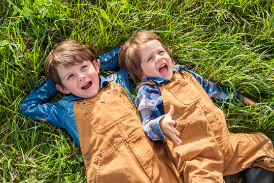 Two brother lie down in a grassy field beside one another