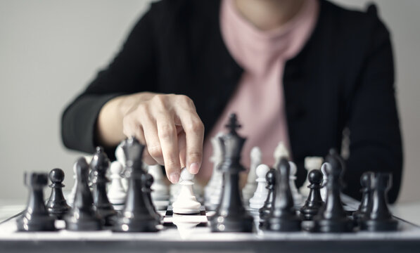 Hand of businesswoman moving white king chess piece on chessboard for business strategy leadership competition and management success concept