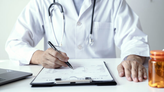 Doctor holding laboratory report document and pen to analyze medical patient health results near laptop on desk in hospital clinic office space