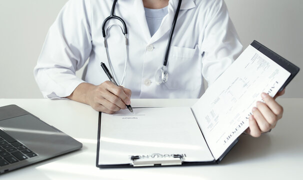 Doctor holding laboratory report document and pen to analyze medical patient health results near laptop on desk in hospital clinic office space