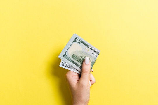 Top view of female hand holding a pack of money on colorful background. One hundred dollars. Business concept with empty space for your design. Charity and tips concept