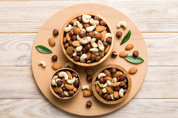 Fototapeta premium Assortment of nuts in wooden bowl on colored table. Cashew, hazelnuts, walnuts, almonds. Mix of nuts Top view with copy space
