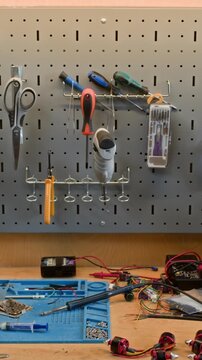 Vertical video of camera zooming out from pegboard with tools to reveal electronics workshop table with soldering iron and wires. Clip is ideal for engineering education or hardware startup promos