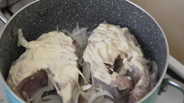 Cod fish preparation with white onions and creamy sauce inside a kitchen pot. Static high angle shot.
