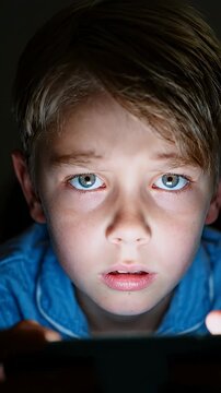Close-up Of Child's Eyes Watching Smartphone Screen In Darkness - A young Caucasian boy is captivated by the content on his smartphone, his eyes wide and reflecting the screen's glow.