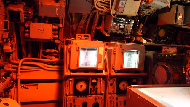 Vintage submarine control room with red lighting and analog radar screens.