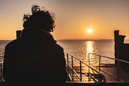 Contemplative boy watching the orange sunset over the lake