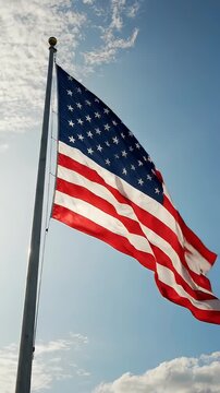 American Flag Waving Against a Cloudy Sky - A vibrant American flag billows in the wind against a clear blue sky with scattered white clouds.