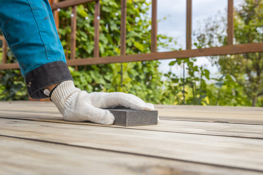 Person sands wooden deck with hand tool