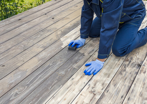 Worker sands weathered wooden deck