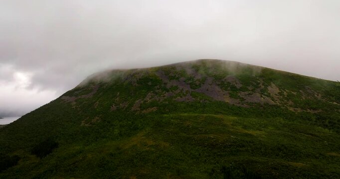 Low cloud and mist drifting across a green mountain near Sortland in Vester&aring;len, Northern Norway, creating a dramatic landscape, cinematic aerial view