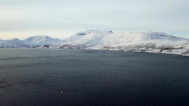 Snow-covered mountains surround fjord with aquaculture salmon farm marine pens